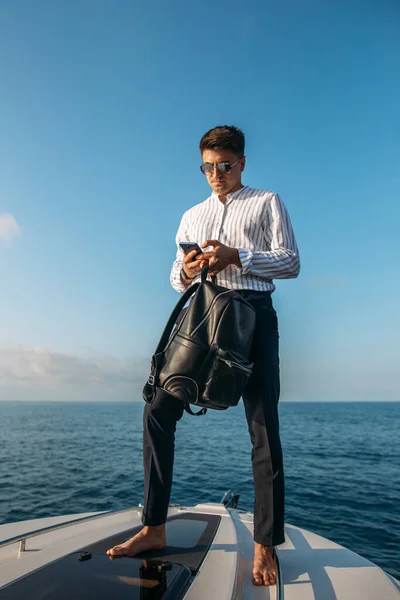 Serious confident handsome mature yacht owner in blue life jacket leaning on boom and looking at camera while sailing in sea