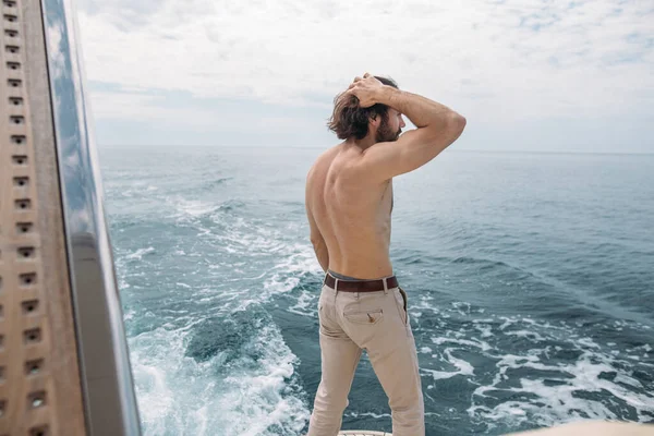 Вид сзади на молодого человека, сидящего на краю яхты, смотрящего на море — стоковое фото