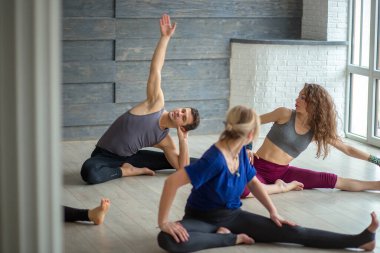 Bir grup beyaz tenli çekici insan iyi ışıklandırılmış stüdyoda yoga yapıyor..