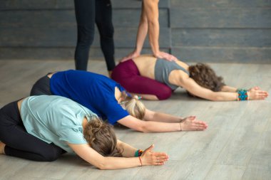 Stüdyoda eğitmen rehberliğinde yoga yapan bir grup beyaz kadın.