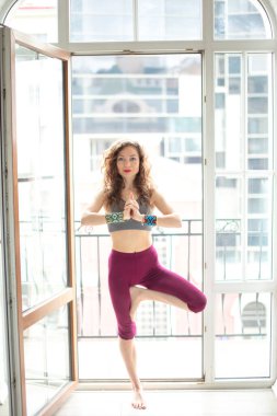 Stüdyoda çalışan zayıf bir kadın, büyük Fransız penceresine karşı yoga egzersizi yapıyor.