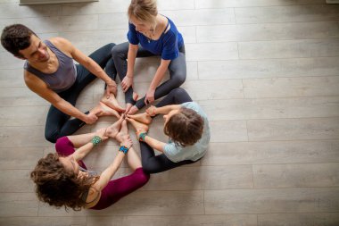 İnsanlar yoga seminerinde meditasyon yapıyor, el ve bacakları bir arada tutuyor.