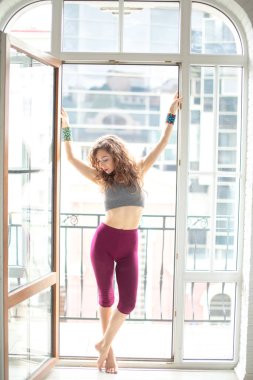 Stüdyoda çalışan zayıf bir kadın, büyük Fransız penceresine karşı yoga egzersizi yapıyor.