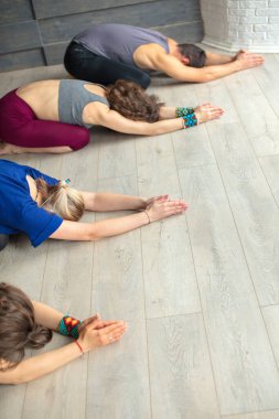 Stüdyoda eğitmen rehberliğinde yoga yapan bir grup beyaz kadın.
