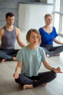 Yoga yapan konsantre insanlar stüdyoda yarım Lotus egzersizi yapıyor.