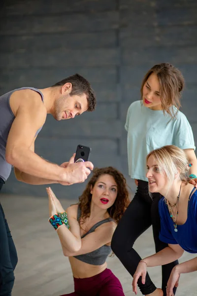 スポーツウェアのスポーツマンはヨガクラスの女の子にスマートフォンを介して写真を示す — ストック写真
