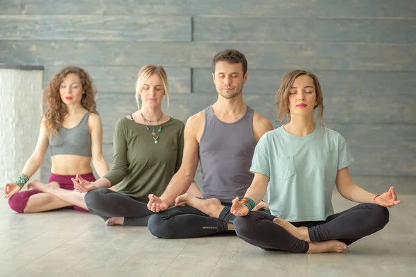 Mujeres jóvenes y hombres meditando mientras practican yoga en una sala de entrenamiento. Concepto de libertad. Calma y relax, felicidad — Foto de Stock