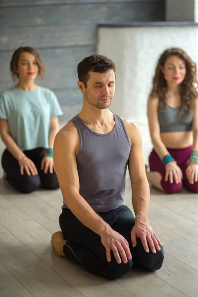 Handsome young muscular man, yogi teacher conducting yoga to caucasian women.