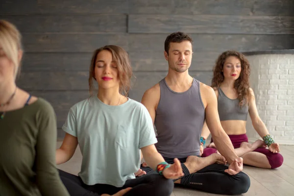 Grupo de jóvenes deportistas que practican clases de yoga, sentados en la pose de Sukhasana — Foto de Stock