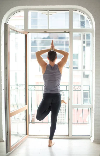 Sporty άνθρωπος εξάσκηση γιόγκα σε λευκό δωμάτιο με μεγάλο παράθυρο. στάση δένδρου — Φωτογραφία Αρχείου