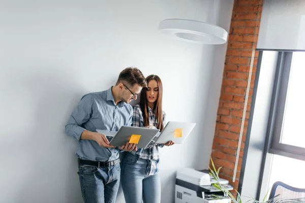 Gelukkig mix-race paar houden laptop computer terwijl staande en vieren geïsoleerd over grijze muur achtergrond — Stockfoto