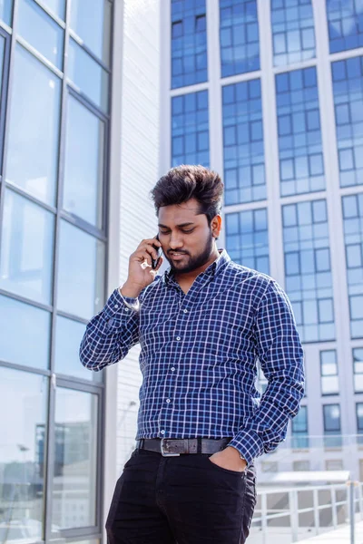 Indian man in casual cloth with beard calling in front of an office building.