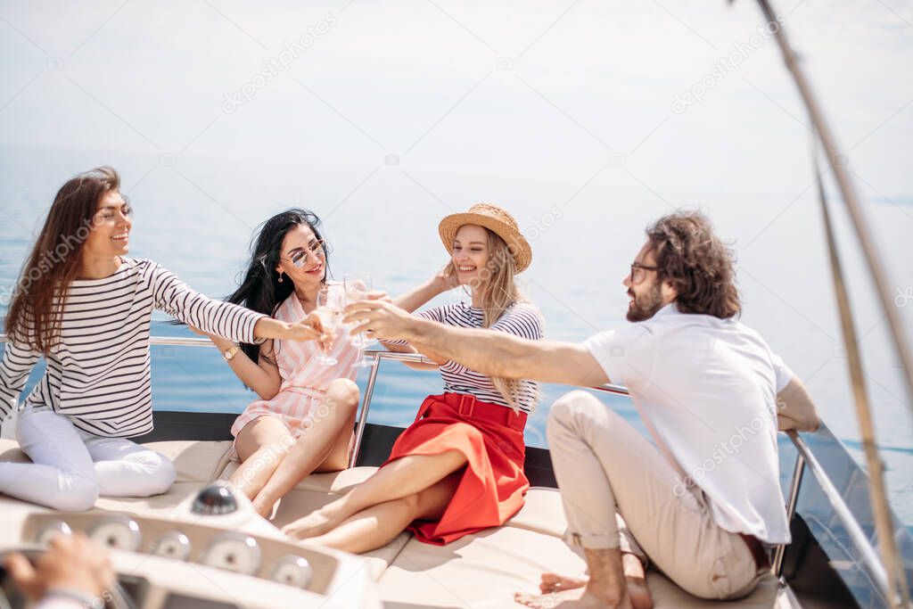 Happy friends clinking glasses of champagne and sailing on yacht