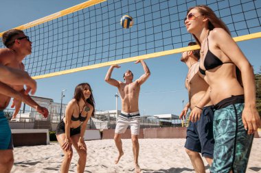 Bir grup genç plajda voleybol oynuyor.