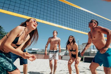 Kumsalda voleybol oynayan bir grup genç.