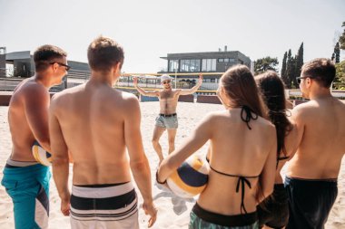 Bir grup arkadaş güneşli bir sabahta voleybol sahasında yürüyorlar..