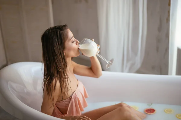 Чуттєва приваблива жінка, що розслабляється у ванні зі склянкою молока . — стокове фото
