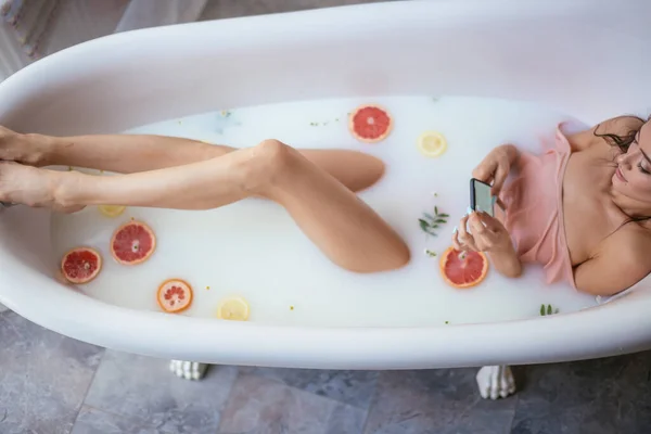 Mujer bonita usando el teléfono móvil mientras toma un baño en casa — Foto de Stock