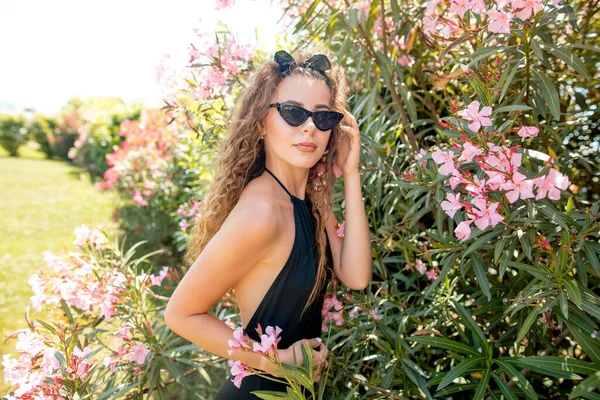 Mujer joven posando en la suite de natación contra arbustos con rosas rosadas. —  Fotos de Stock