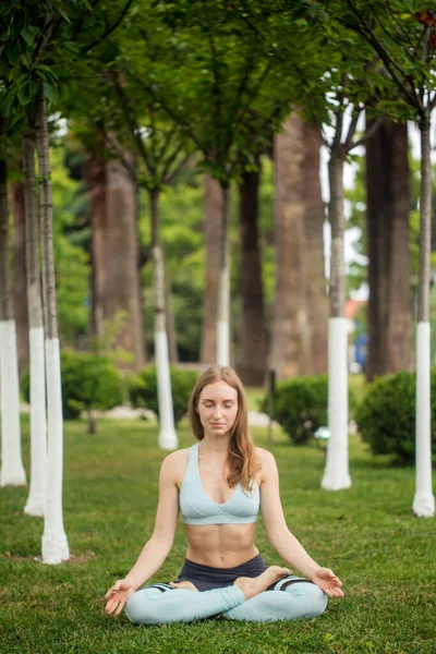 Güzel genç bir kadın parkta yoga yapıyor ve namaste mudra yapıyor. — Stok fotoğraf