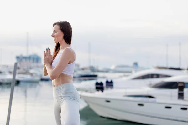 Kvinna som gör yoga vid piren. Kvinna avkopplande vid havet docka i träd pose. — Stockfoto