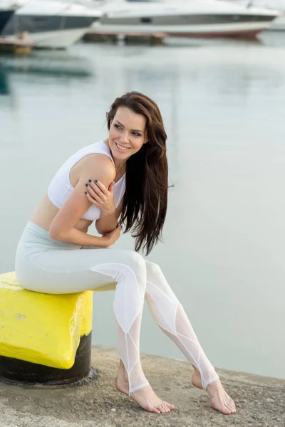 Young sportive woman is sitting on sea, marina pier and looking at horizon — Stock Photo, Image