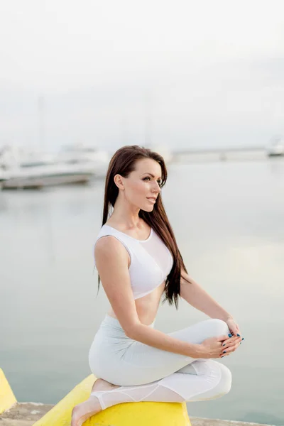 Молодая спортивная женщина сидит на море, пристани для яхт и смотрит на горизонт — стоковое фото