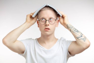 Beyaz adam gülümser ve yüzünü bir kitabın arkasına saklar. Stüdyo resmi