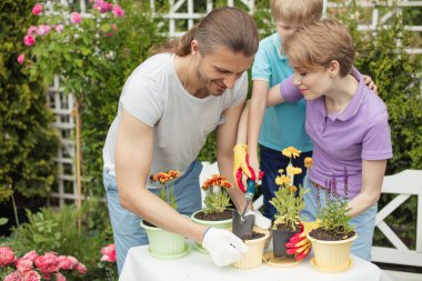 Genç anne, iki tatlı çocuğuyla bahçede bahçeyle uğraşıyor.