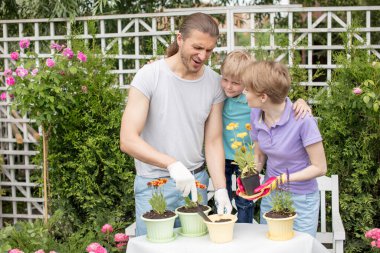Genç anne, iki tatlı çocuğuyla bahçede bahçeyle uğraşıyor.