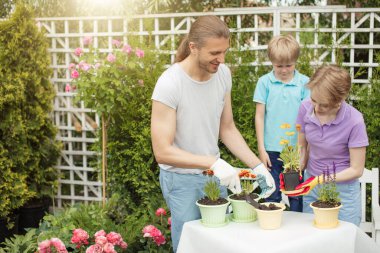 Genç anne, iki tatlı çocuğuyla bahçede bahçeyle uğraşıyor.