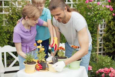 Genç anne, iki tatlı çocuğuyla bahçede bahçeyle uğraşıyor.