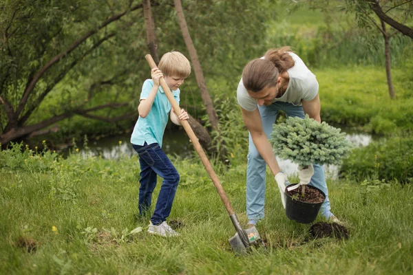 Sorrindo pai adulto e seu filho plantando uma árvore ao ar livre no parque. — Fotografia de Stock