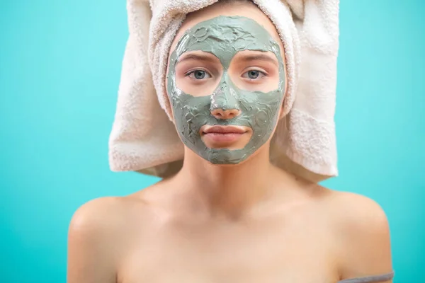 Mujer con toalla en la cabeza aplicando mascarilla facial de arcilla. — Foto de Stock