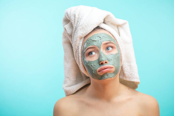 Unhappy teenager female with black clay face mask makes acne therapy in spa
