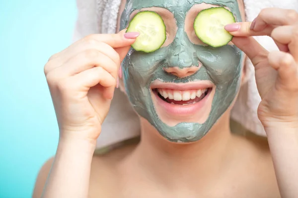 Mujeres jóvenes con máscaras faciales y rodajas de pepino aisladas sobre la pared azul del estudio — Foto de Stock