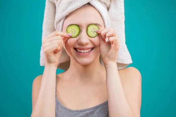 Mujer con una toalla en la cabeza divirtiéndose, cubriendo los ojos con rodajas de pepino. —  Fotos de Stock