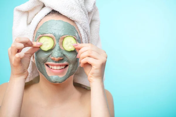 Mujeres jóvenes con máscaras faciales y rodajas de pepino aisladas sobre la pared azul del estudio — Foto de Stock