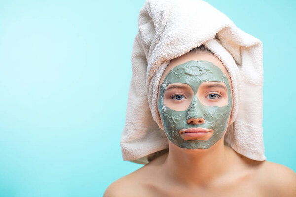 Unhappy teenager female with black clay face mask makes acne therapy in spa