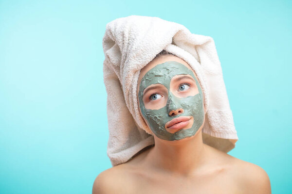 Unhappy teenager female with black clay face mask makes acne therapy in spa