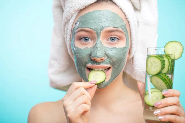 Pozitivní usmívající se dívka s hliněnou kosmetickou maskou a organickými okurkovými plátky — Stock fotografie