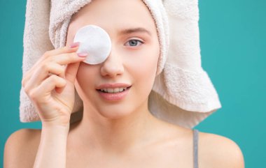 Beyaz kadın mavi arka planda izole edilmiş pamuk yüz temizleyici disk kullanıyor.