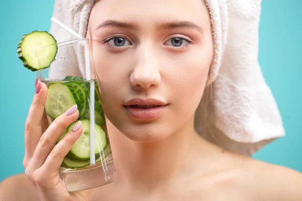 Mujer spa con toalla en la cabeza sosteniendo vaso de agua de pepino isoalted sobre azul —  Fotos de Stock