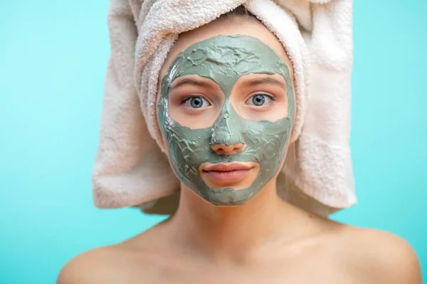 Mujer con toalla en la cabeza aplicando mascarilla facial de arcilla. — Foto de Stock