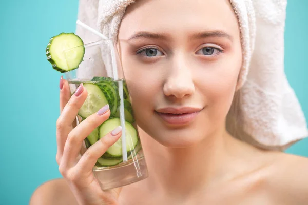 Mujer spa con toalla en la cabeza sosteniendo vaso de agua de pepino isoalted sobre azul —  Fotos de Stock