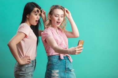 Mutlu genç kızlar mavi duvara karşı akıllı telefonlarıyla selfie çekiyorlar.