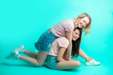 İki çok ırklı kadın mavi arka planda sırt sırta oturuyorlar.