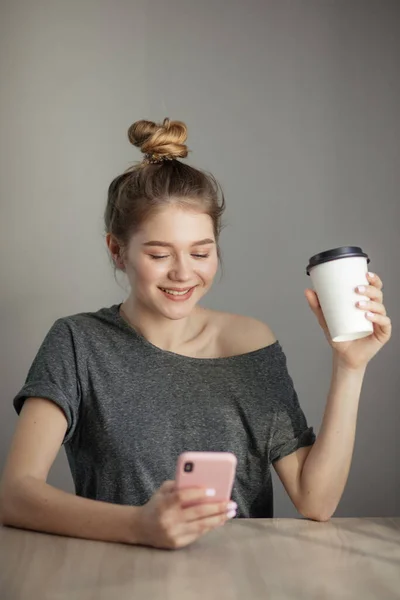 young woman sitting at a table with a coffee using mobile phone.
