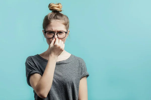 Mladá dívka mačkat nos s prsty, dívá se do kamery s odporem. — Stock fotografie