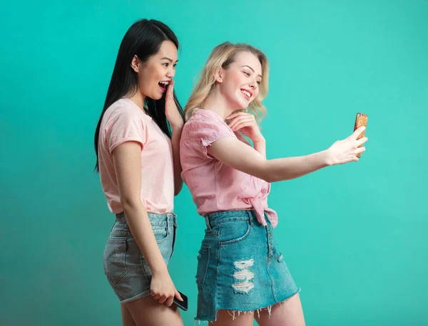 Dos multiétnicas hermosas mujeres asiáticas y caucásicas tomando selfie en estudio — Foto de Stock